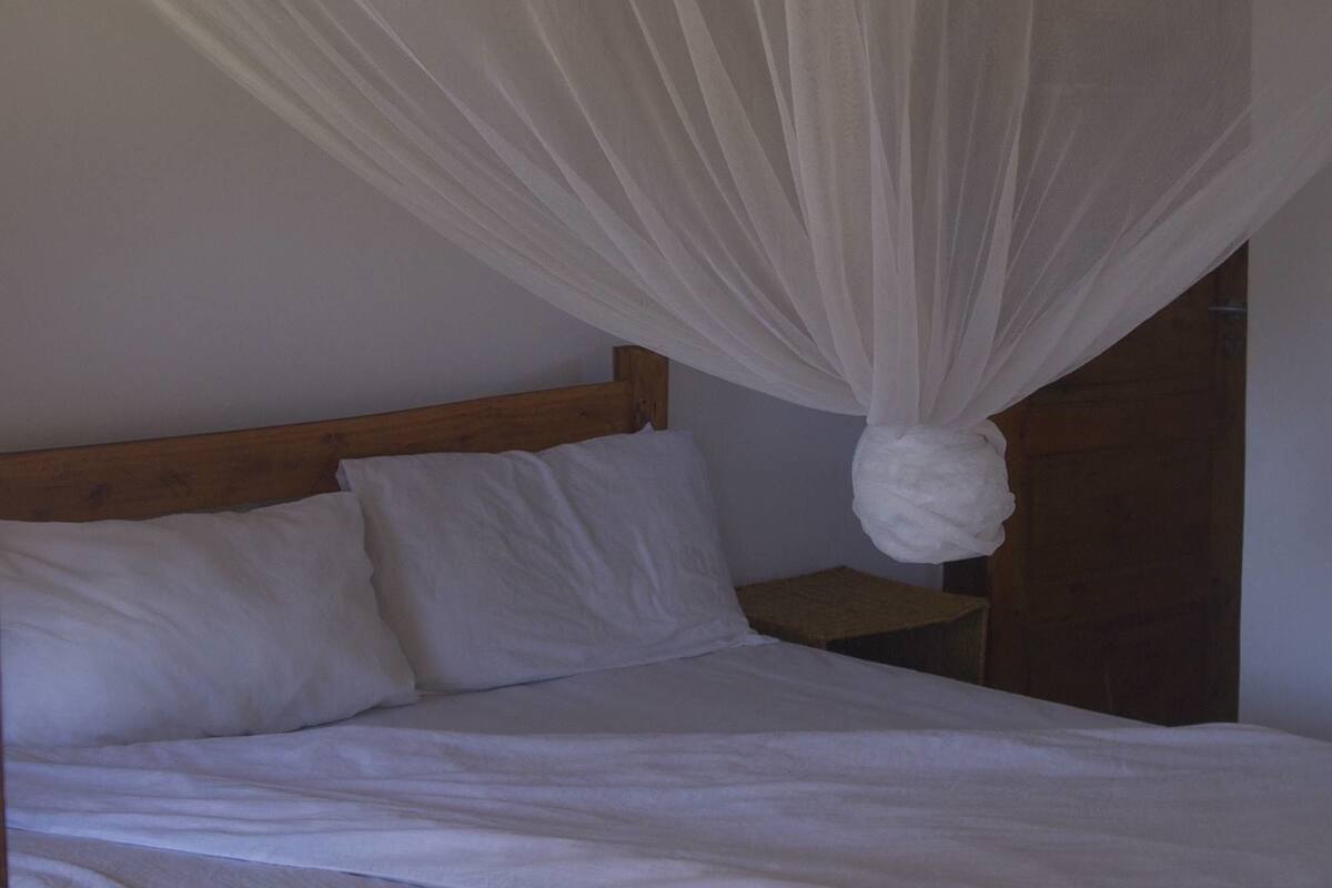 Una cama con dosel, cabecera de madera y ropa de cama blanca.