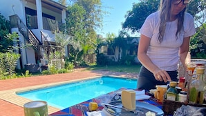 Una mesa de comedor con alimentos para el desayuno, una piscina y un edificio al fondo.