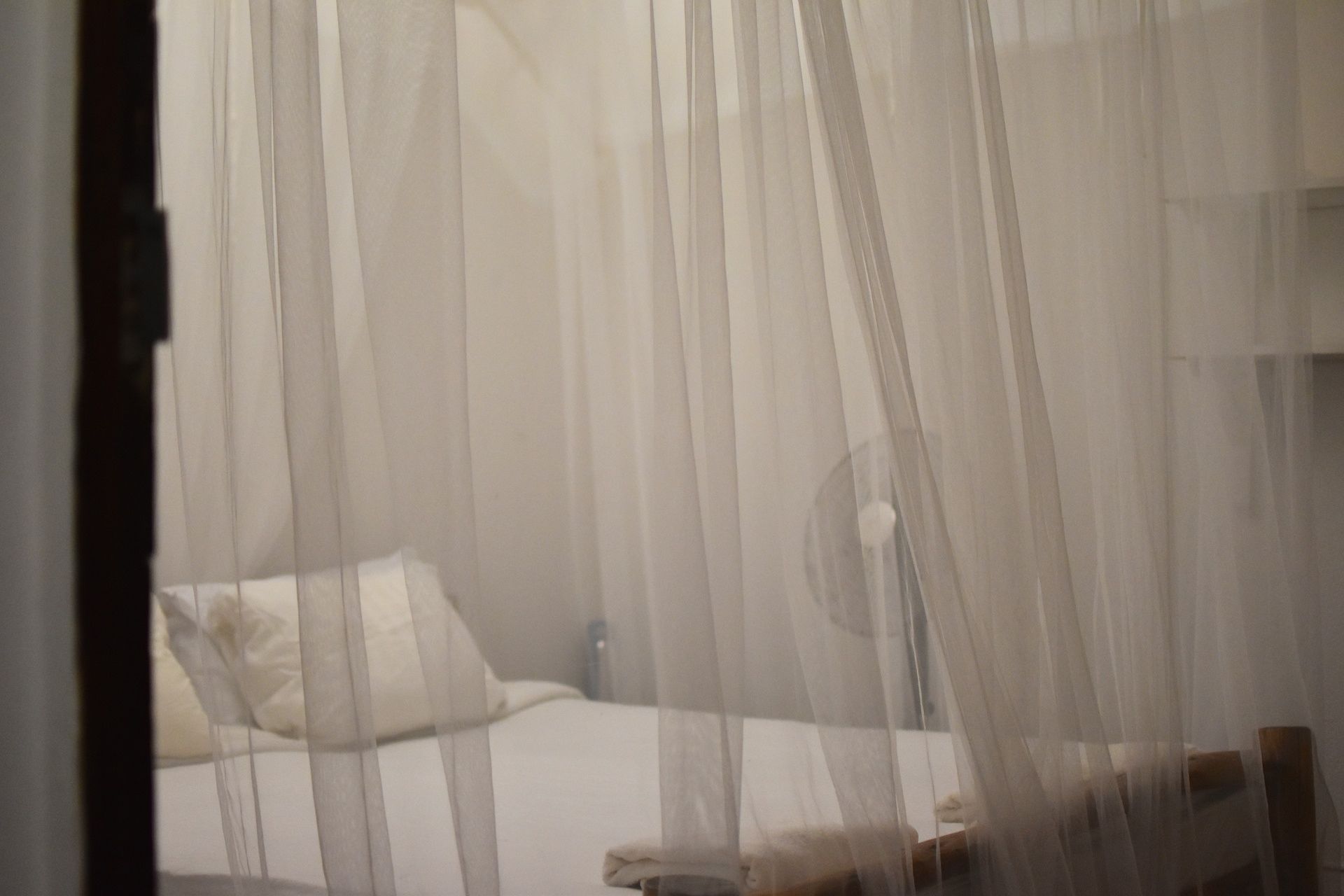 Una cama con colchón y almohadas blancas, parcialmente cubierta por cortinas traslúcidas.