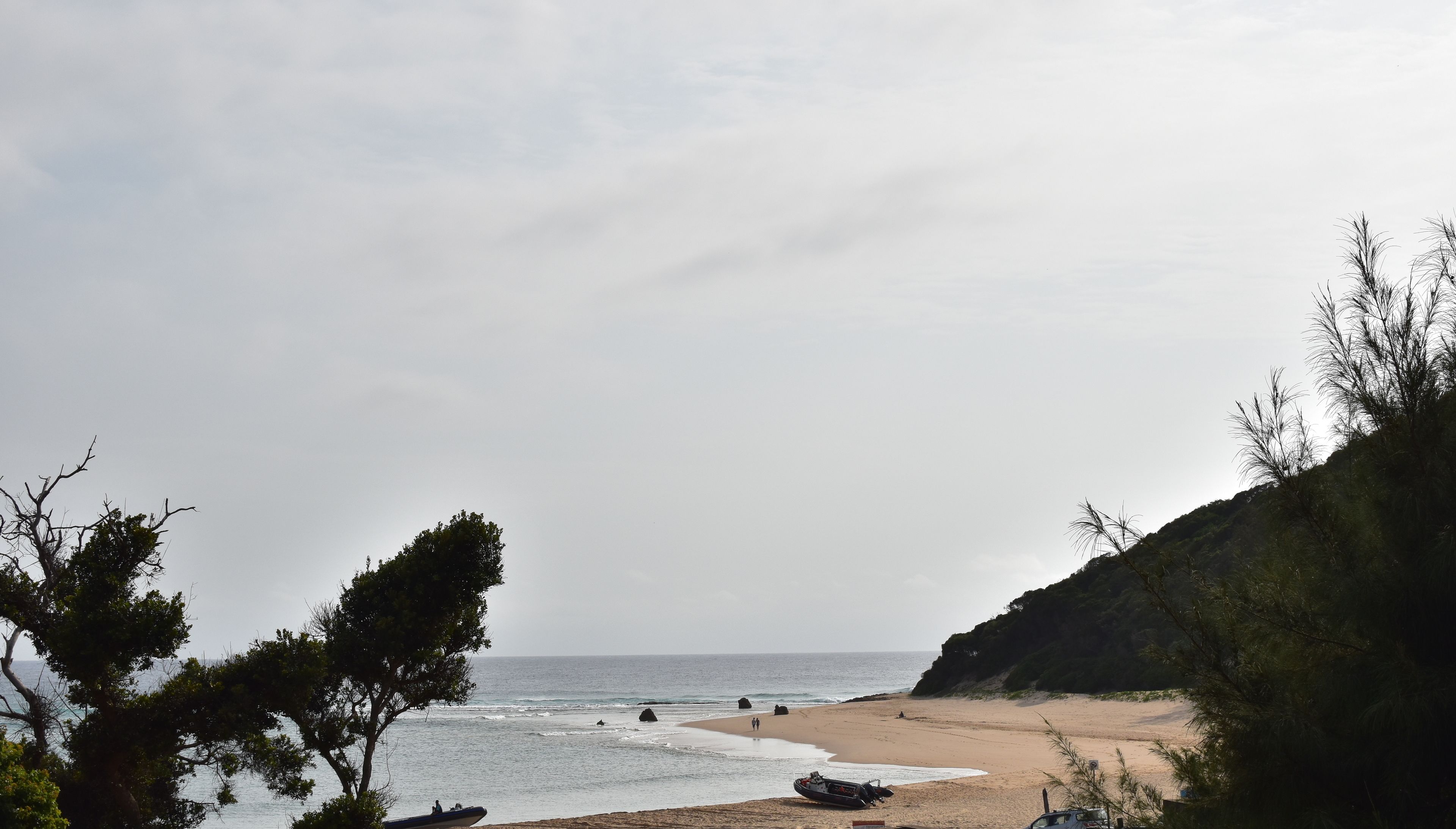 Una playa con un bote, algunas personas y un acantilado.