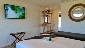 A modern room with a large flat-screen TV, a wooden shelf with a mirror, a round mirror, a black sofa, and a small table with toiletries. - Vacy Hunter Valley Lodge (Vacy)