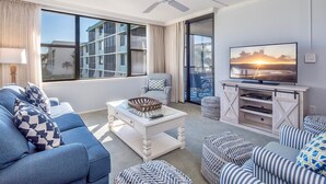 Ein Wohnzimmer mit einer Couch, Hocker, einem Couchtisch, einem Fernseher und einem Deckenventilator.
