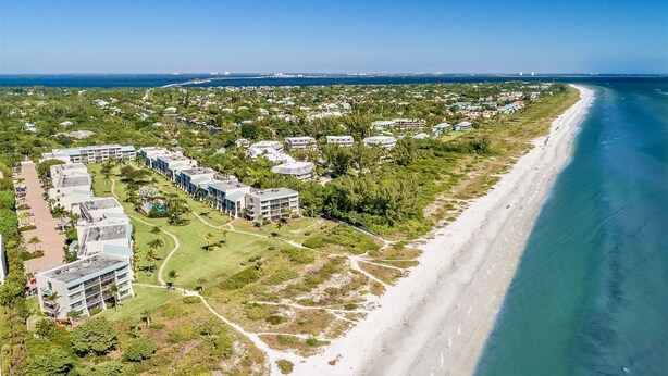 Luftaufnahme eines Küstenresorts mit mehreren Gebäuden, einem Strand und blauem Himmel.
