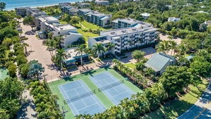 Eine Luftaufnahme eines Resorts mit mehreren Gebäuden, einem Tennisplatz und einem Strand im Hintergrund.