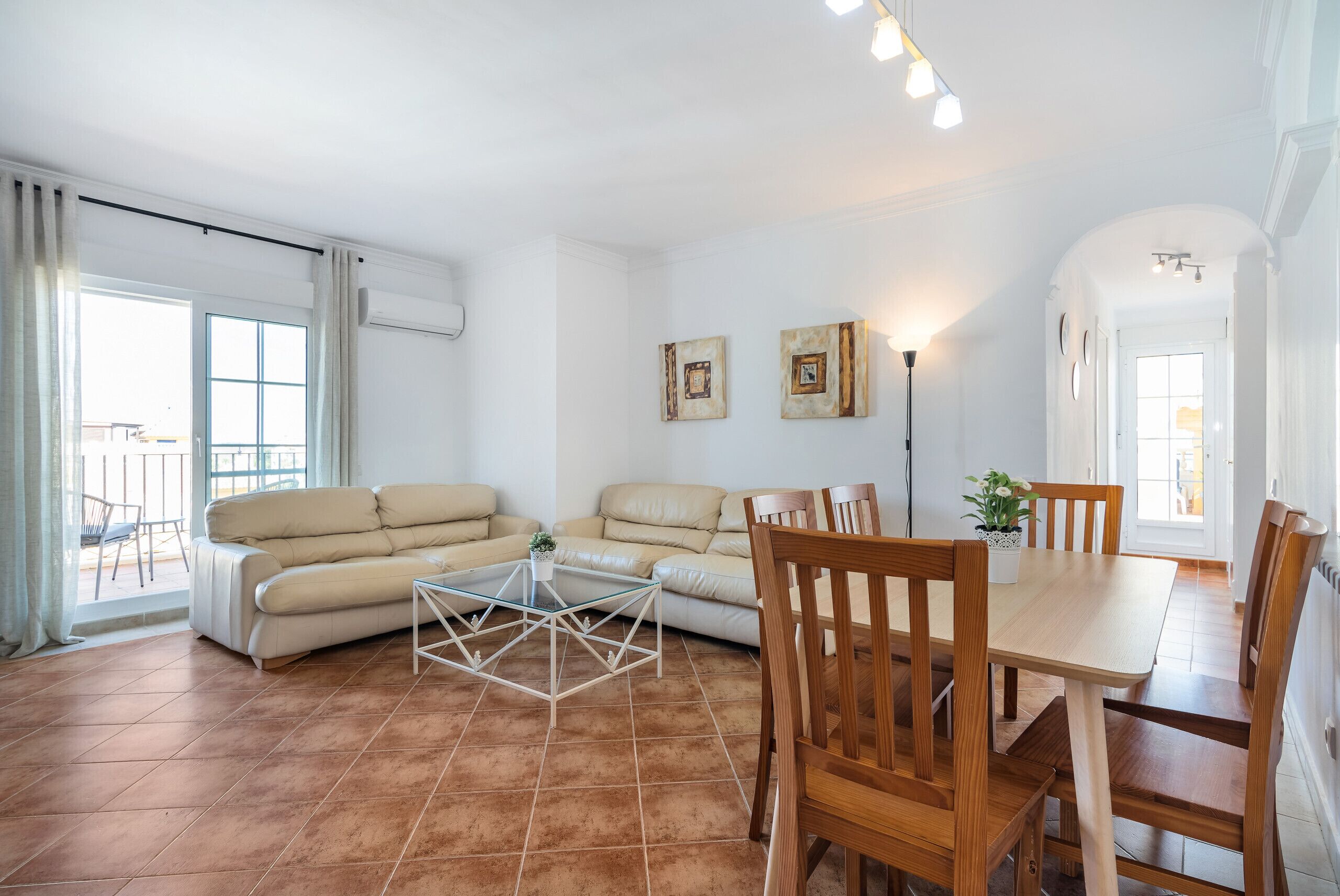 Una sala de estar con un sofá, una mesa de centro de vidrio, sillas de madera, una mesa de comedor y una planta en maceta.