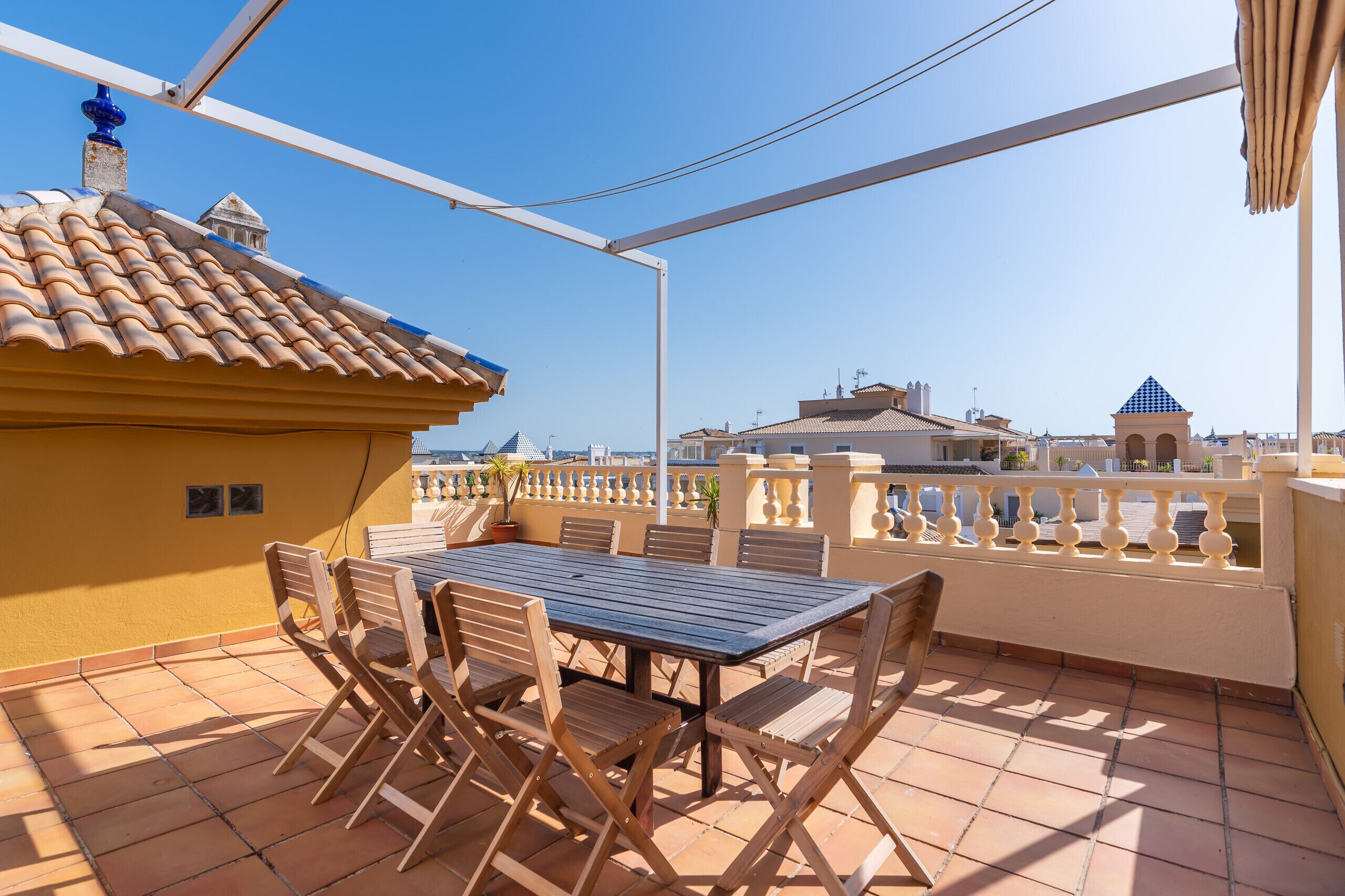 Une terrasse avec une table et des chaises, un toit en tuiles et une vue sur les bâtiments en arrière-plan.