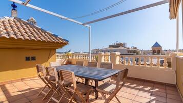 Une terrasse avec une table et des chaises, un toit en tuiles et une vue sur les bâtiments en arrière-plan.
