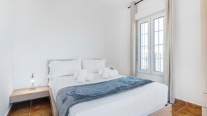 A bedroom with a bed, pillows, a bedside table with a lamp, and a window with curtains. - Playa Grande PLUS - Punta del Moral Beach PPHG207P209 (Punta del Moral)