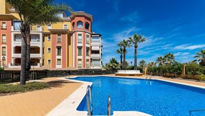 A swimming pool with a clear blue sky, palm trees, and multi-story buildings in the background. - Playa Grande PLUS - Punta del Moral Beach PPHG207P209 (Punta del Moral)