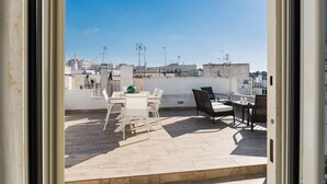 A rooftop terrace with a table and chairs, a view of the cityscape, and a clear sky.