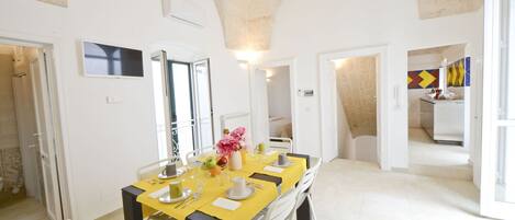 A dining area with a yellow table, white chairs, and a vase with flowers.