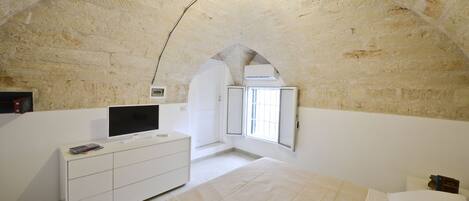 A bedroom with a stone ceiling, a bed, a TV on a white dresser, and a window with a view.