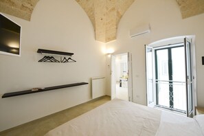 Une chambre à coucher comprenant un lit, un radiateur, une étagère avec des cintres et une porte donnant sur une autre pièce.