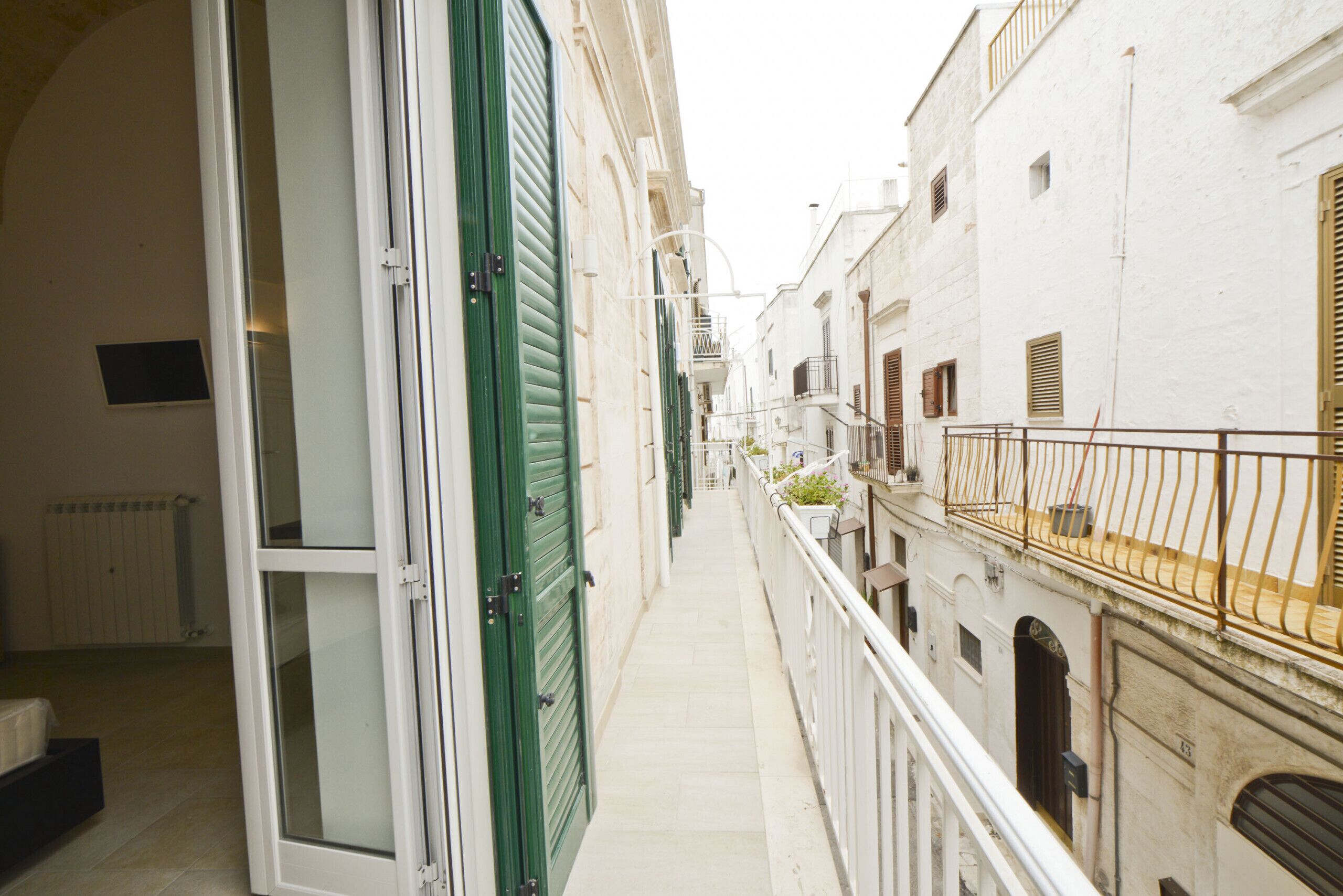 A narrow alleyway with buildings on either side, featuring balconies with railings and a few potted plants.