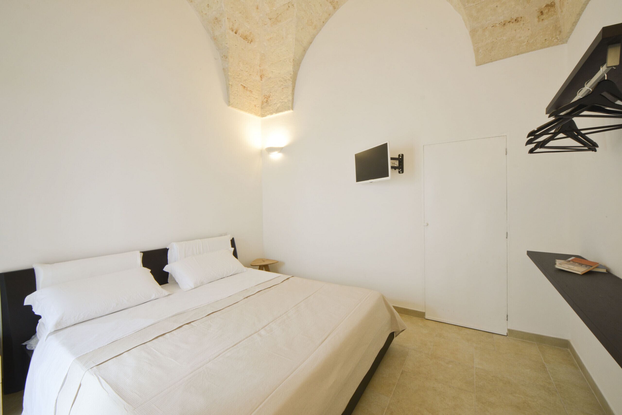A bedroom with a bed, a wall-mounted TV, and a door.
