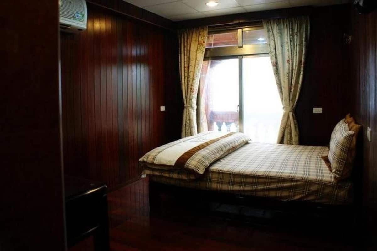 A bedroom with a bed, wooden walls, a window with curtains, and a ceiling fan.