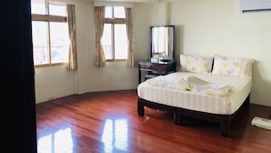 A hotel room with a wooden floor, a bed with striped bedding, a dresser, a mirror, and a window with curtains. - Tophome 9 (New Taipei City)