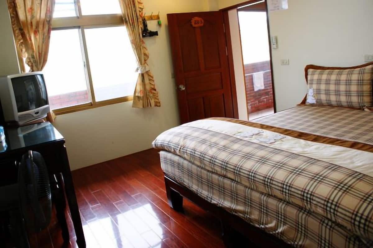 A bedroom with a bed, a television on a stand, and a wooden floor.