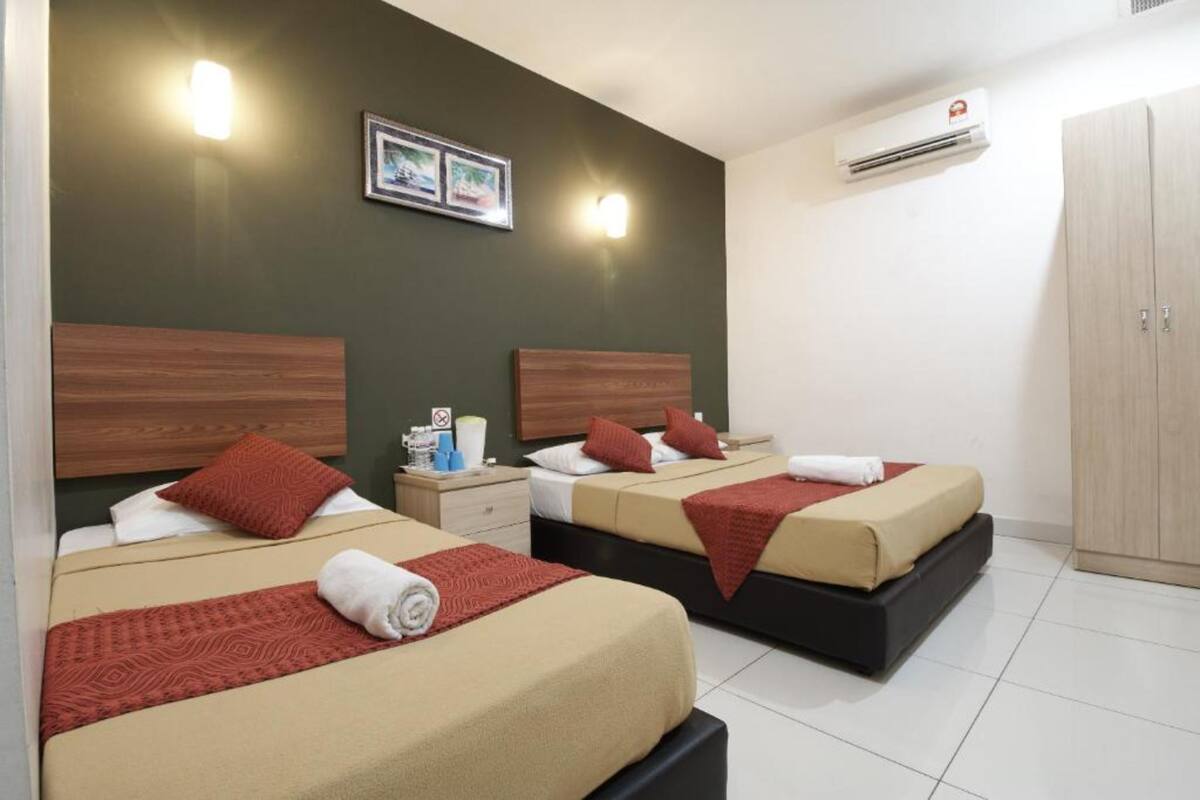 A hotel room with two beds, each with a wooden headboard, a nightstand, and a wall-mounted air conditioner.