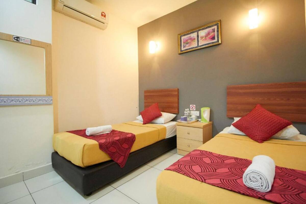 A hotel room with two beds, each with a red and yellow bedspread, a wooden headboard, and a small bedside table with a lamp.