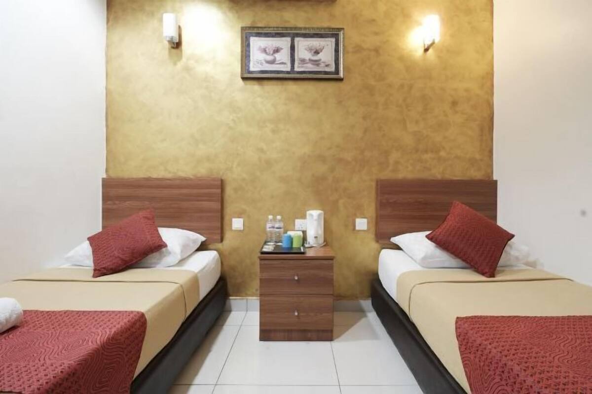 A hotel room with two beds, a wooden nightstand, a framed picture on the wall, and two wall-mounted lights.
