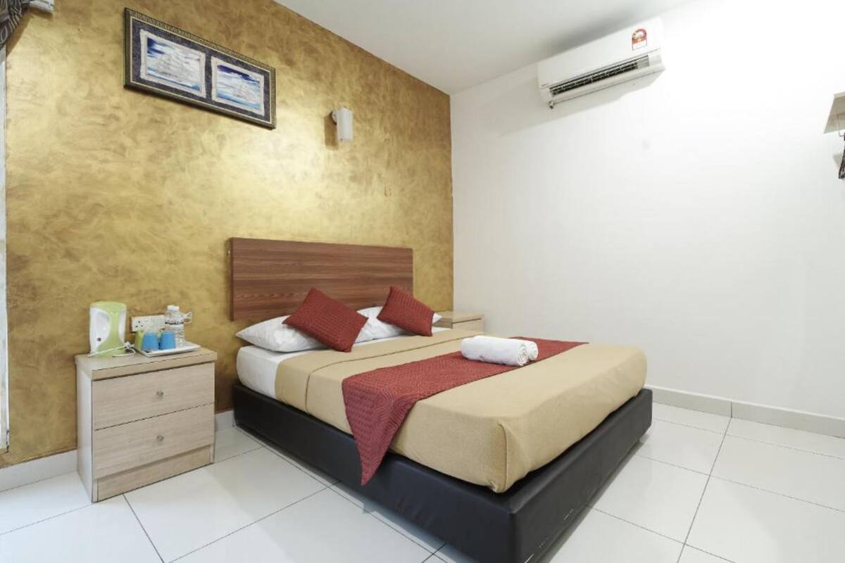 A hotel room with a bed, a nightstand, a wall-mounted air conditioner, and a framed certificate on the wall.