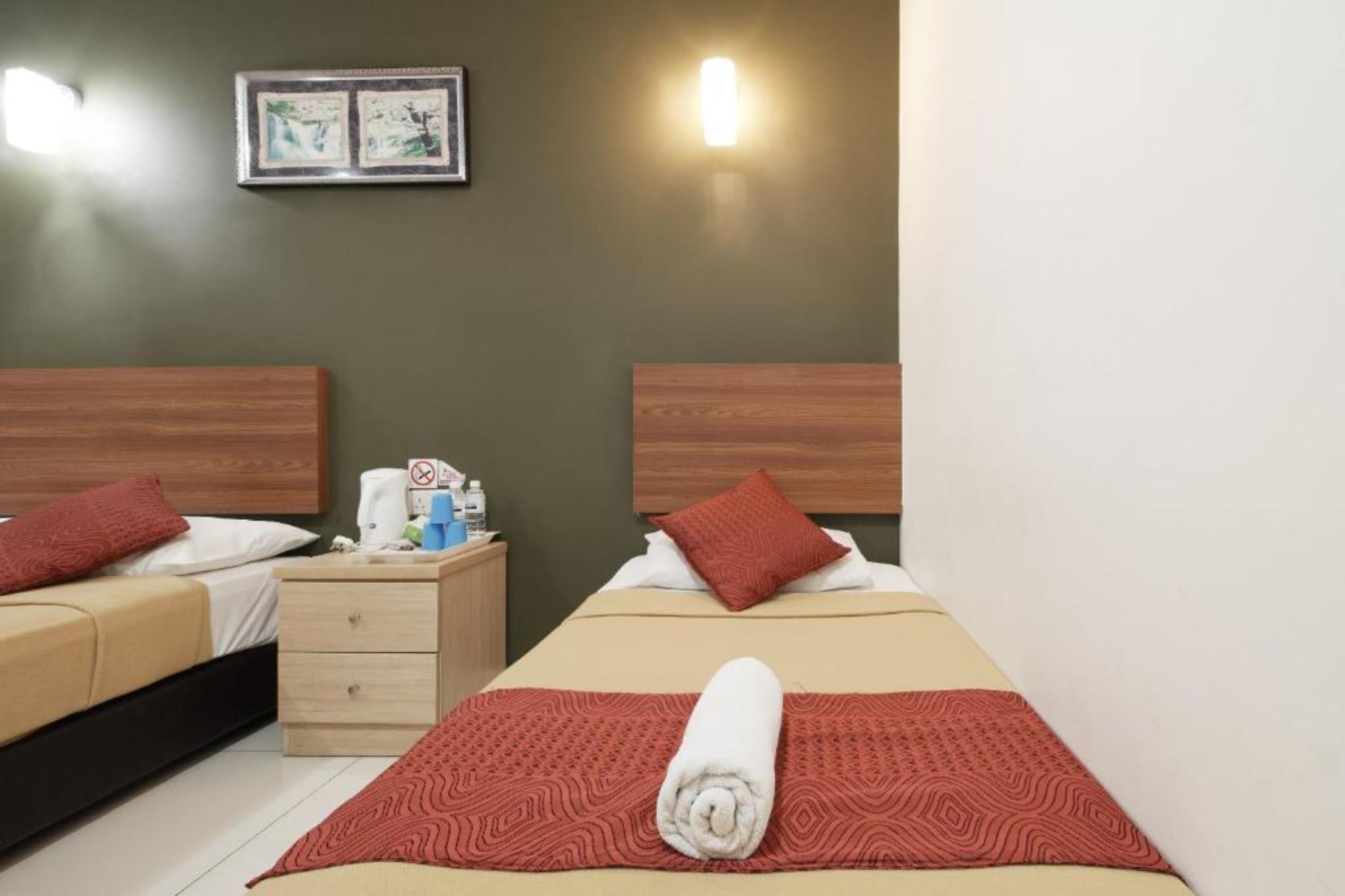 A hotel room with two beds, a nightstand, a wall-mounted light, and a framed picture.
