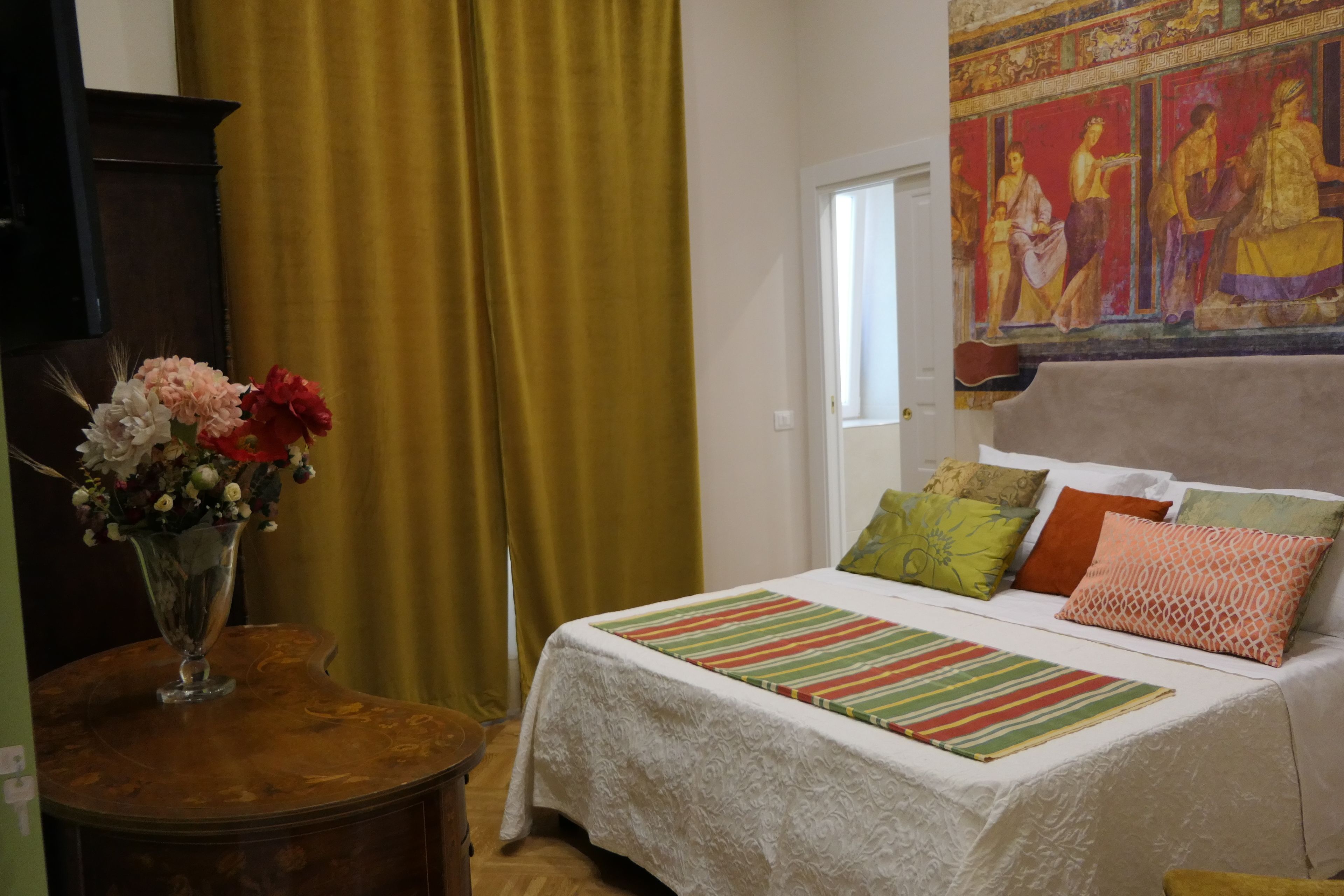 A bedroom with a bed, a vase of flowers, and a painting on the wall.