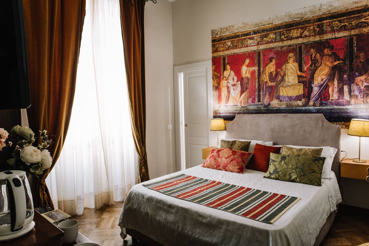 A hotel room with a bed, curtains, a painting, and a lamp.