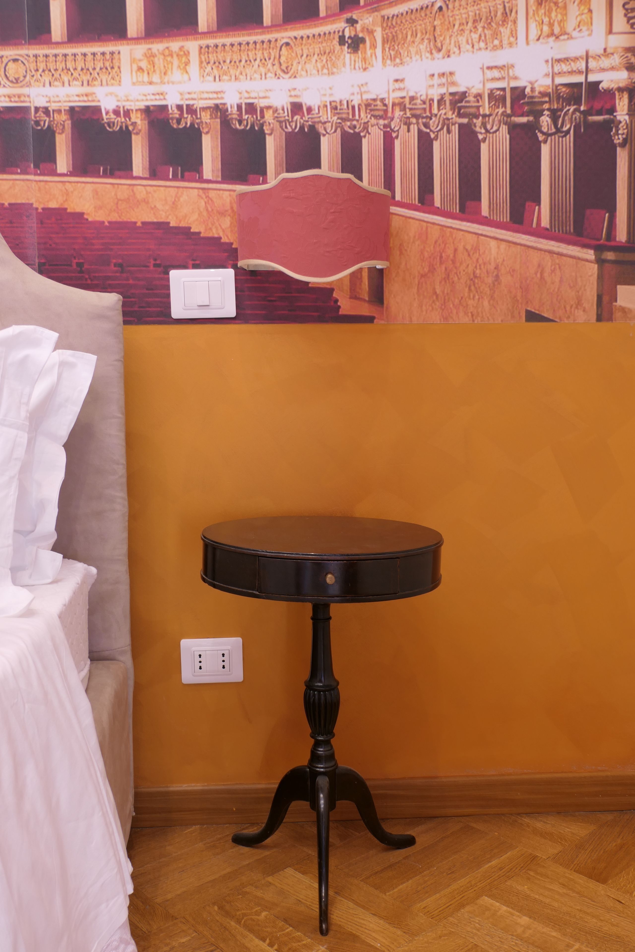Ein Zimmer mit Holzboden, einem runden schwarzen Tisch auf einer Säule, einem beigen Sofa und einem roten Sessel.