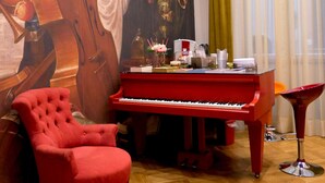 Une pièce avec un piano rouge, un fauteuil rouge et un grand tableau représentant un instrument de musique.