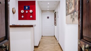 Un couloir avec un comptoir d’accueil, un tableau d’affichage rouge et une porte au fond.