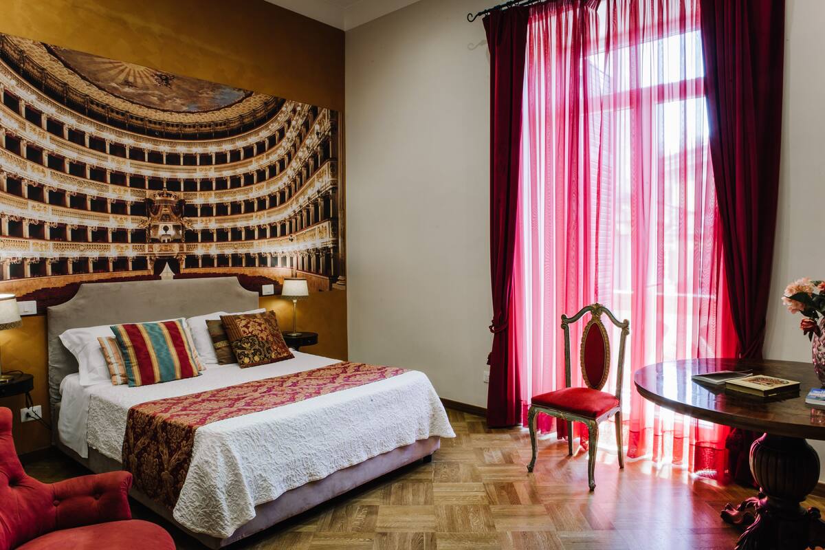A hotel room with a large bed, a red chair, a round table, and a wall mural.