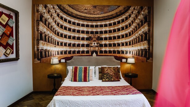Une chambre d’hôtel avec un grand lit, deux tables de chevet, une horloge murale et un tableau encadré.