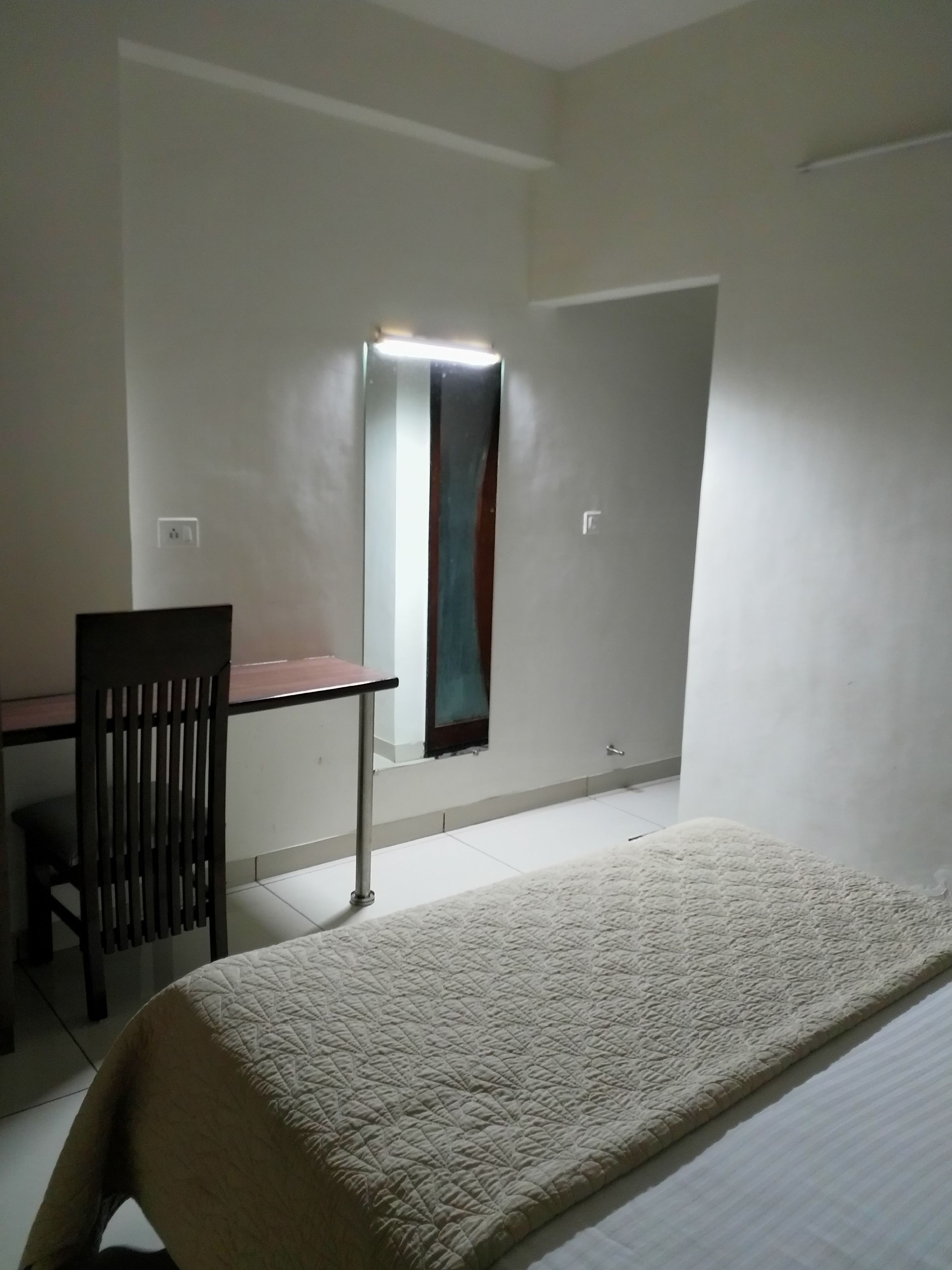 A small, simple room with a bed, a desk, and a chair.