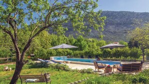 Zona de piscina con sillas de descanso y sombrillas, rodeada de follaje y montañas al fondo.