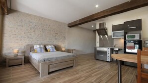Ein Schlafzimmer mit einem Bett, Nachttischen und einem kleinen Schreibtisch mit Stuhl. Es gibt eine Küchenzeile mit Mikrowelle, Herd und Schränken.