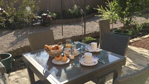 Ein Essplatz im Freien mit Korbstühlen, einem Brotkorb, Tellern mit Essen sowie Tassen und Gläsern.