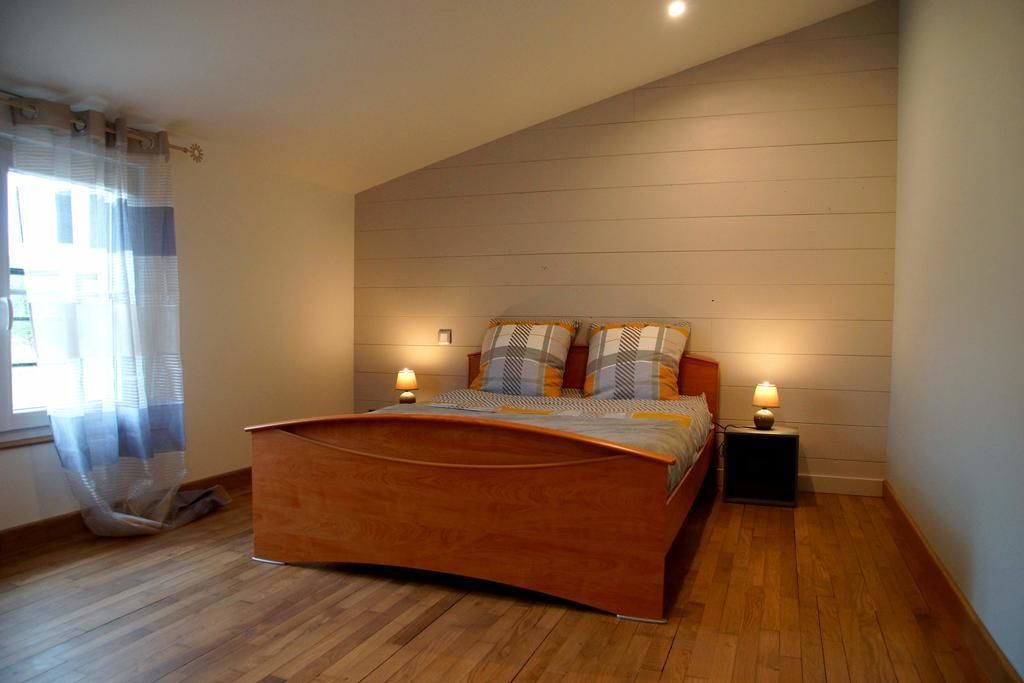 Un dormitorio con una cama de madera, dos mesitas de noche con lámparas y una ventana con cortinas translúcidas.