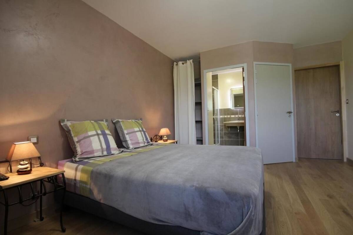 A bedroom with a bed, two bedside tables, a nightstand, a mirror, and a door leading to a bathroom.