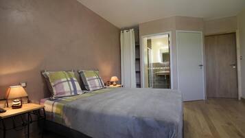 A bedroom with a bed, two bedside tables, a nightstand, a mirror, and a door leading to a bathroom.
