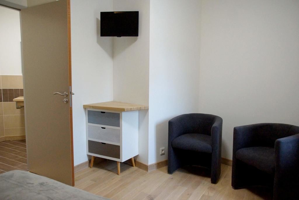 A room with a bed, a desk with drawers, two chairs, and a TV mounted on the wall.