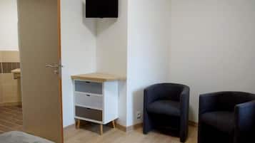 A room with a bed, a desk with drawers, two chairs, and a TV mounted on the wall.