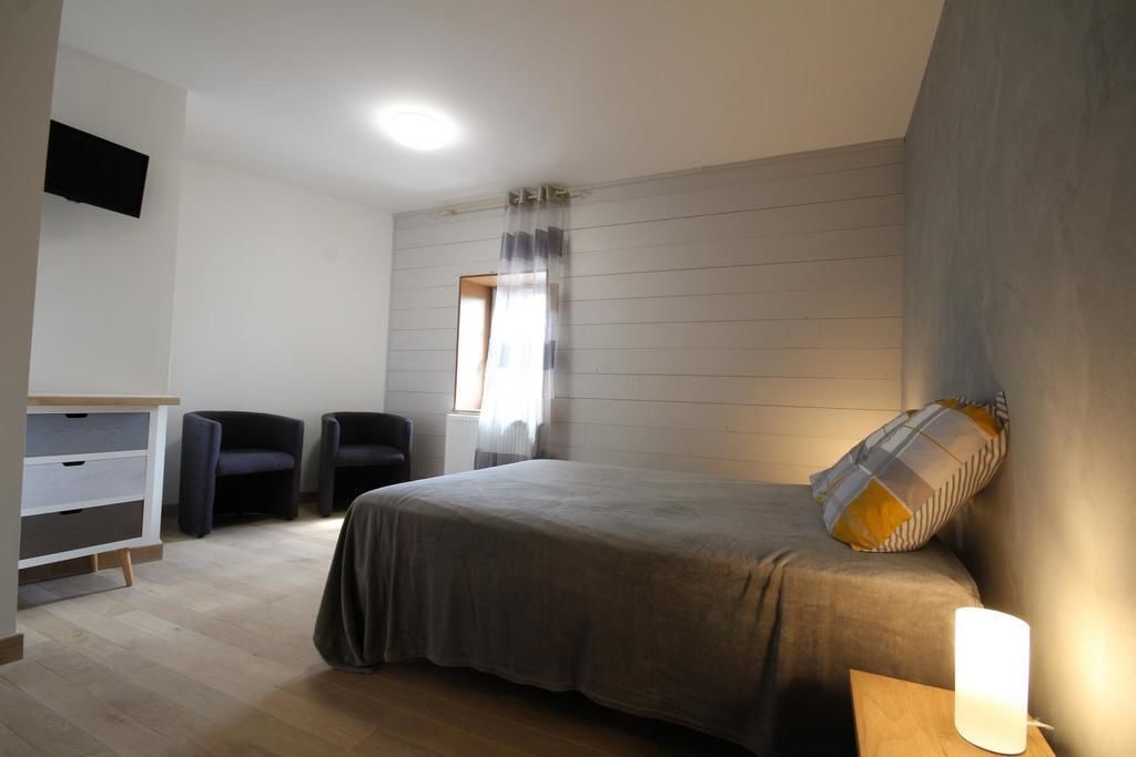 Une chambre à coucher comprenant un lit, un bureau, deux chaises, un téléviseur fixé au mur et une fenêtre avec des rideaux.