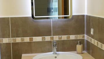 A bathroom with a wooden vanity, a white sink, a mirror, and tiled walls.