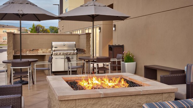 Un patio al aire libre con una chimenea de piedra, zona de parrillada y asientos bajo sombrillas.