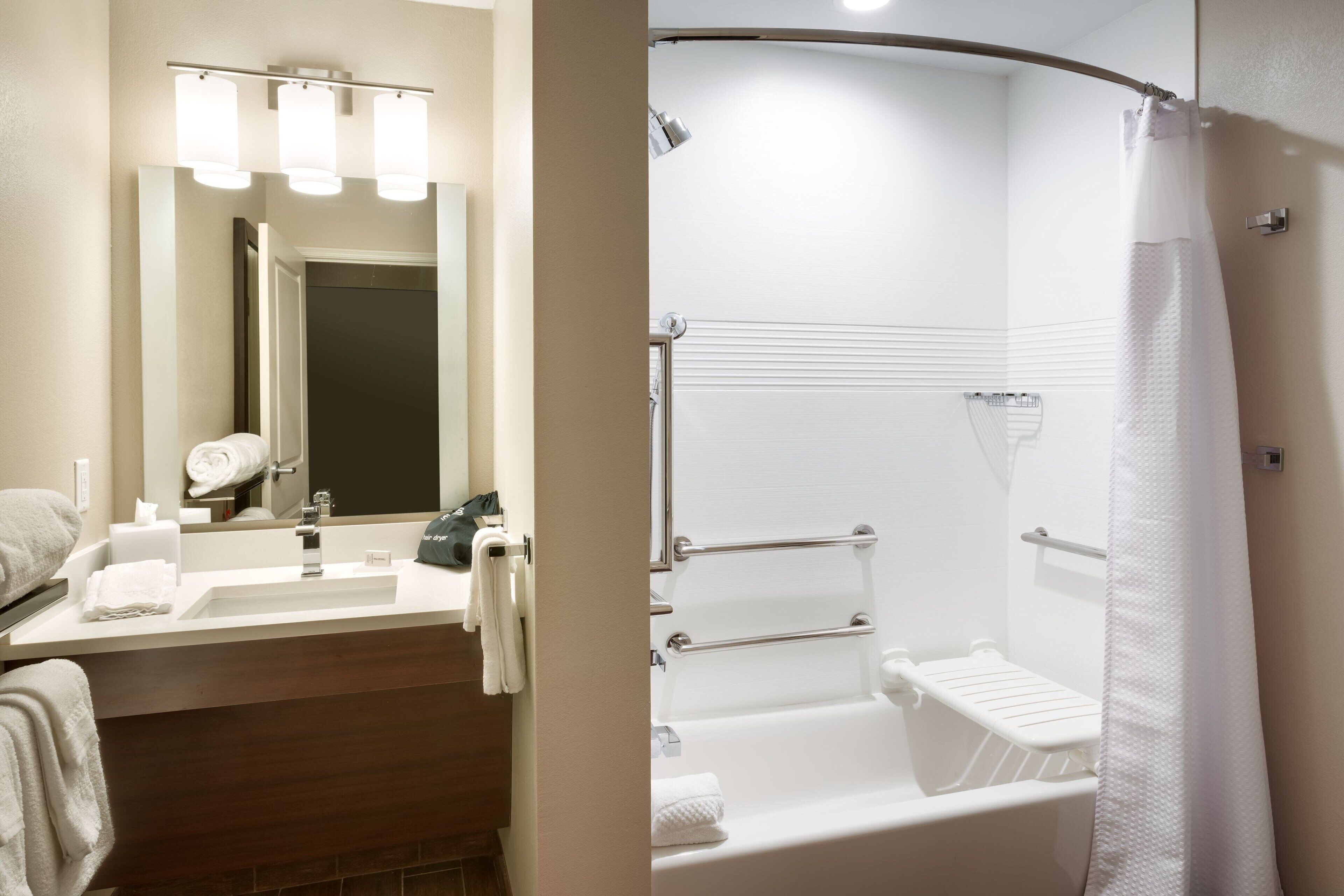 Un baño con lavamanos, espejo, toallero y zona de ducha.
