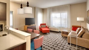 Habitación de hotel con kitchenette, zona de comedor, sofá y televisión.