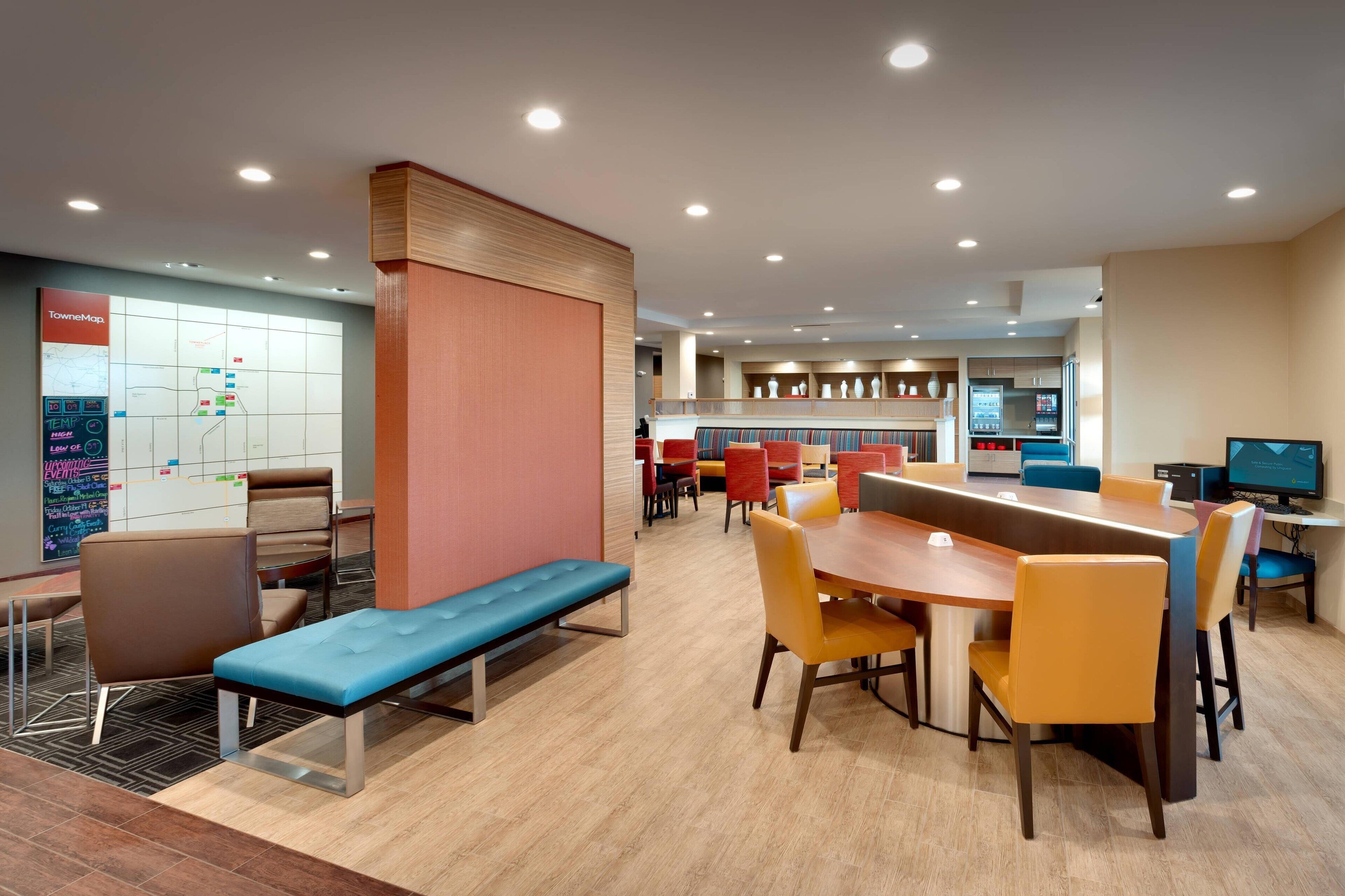 A modern hotel lobby with a long wooden table, multiple seating areas, and a map on the wall.