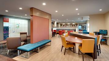 A modern hotel lobby with a long wooden table, multiple seating areas, and a map on the wall.